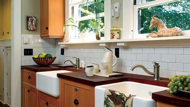 Fir cabinets join mahogany countertops and a backsplash of subway tiles. A pair of farmhouse sinks was installed under the windows with a dishwasher hidden in between.