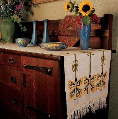 A Stickley Brothers sideboard in the dining room holds a collection of Roseville, Van Briggle, and Rookwood pottery, all set on an antique runner embroidered with stylized dragonflies.