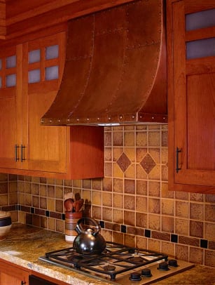 Ceramic tiles in the backsplash are enlivened by tumbled stone and bronze liner tiles. A copper hood is warm and practical.