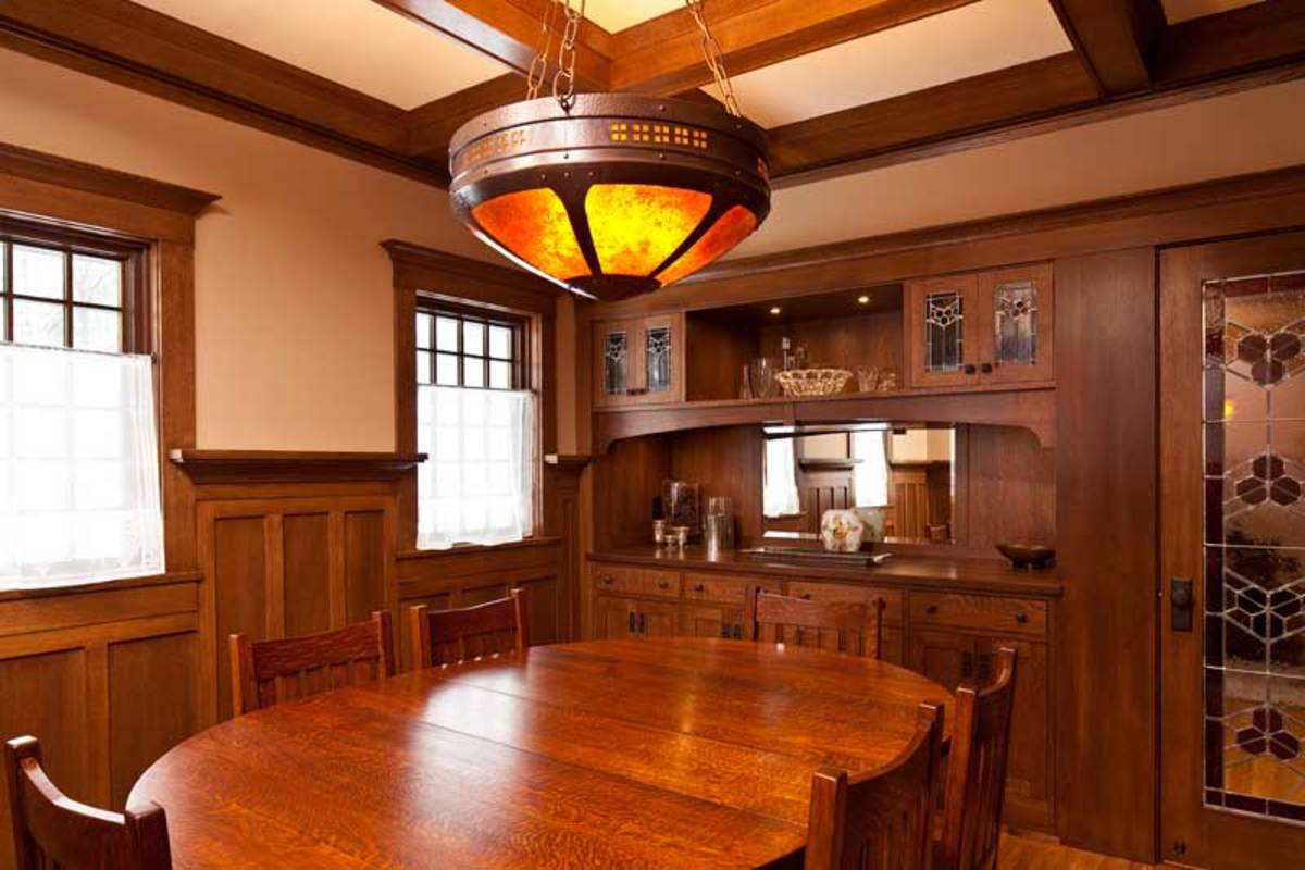 The beamed dining room has a large, six-panel, up-lit mica fixture made by James K. Davies of Craftsman Copper. The built-in sideboard is typical of Arts & Crafts houses. Leaded art glass has a trefoil motif that repeats throughout the house.