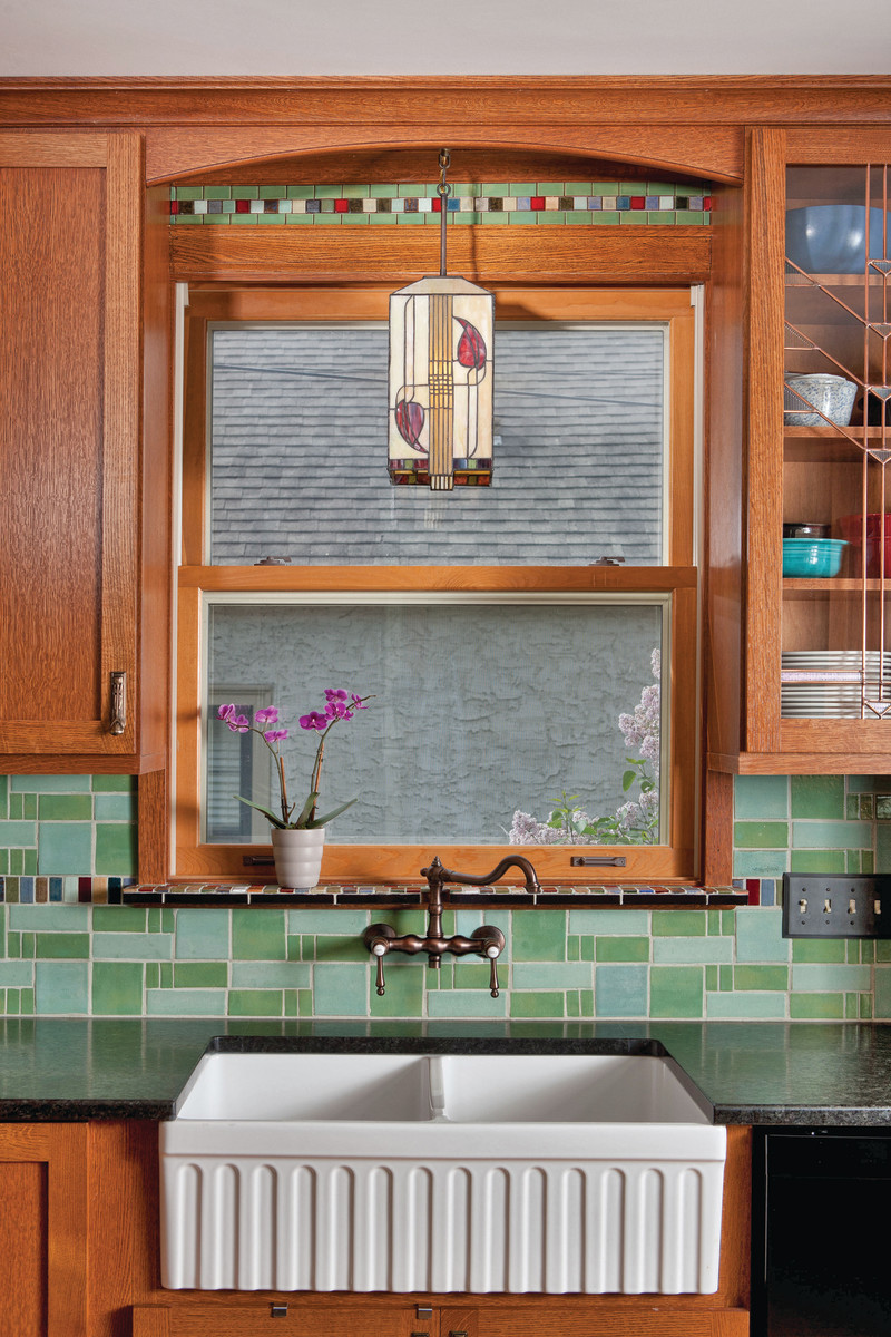 A kitchen backsplash in varying greens picks up a rhythmic quality from different tile sizes, enhanced by a custom strip of small, bright-colored tiles.